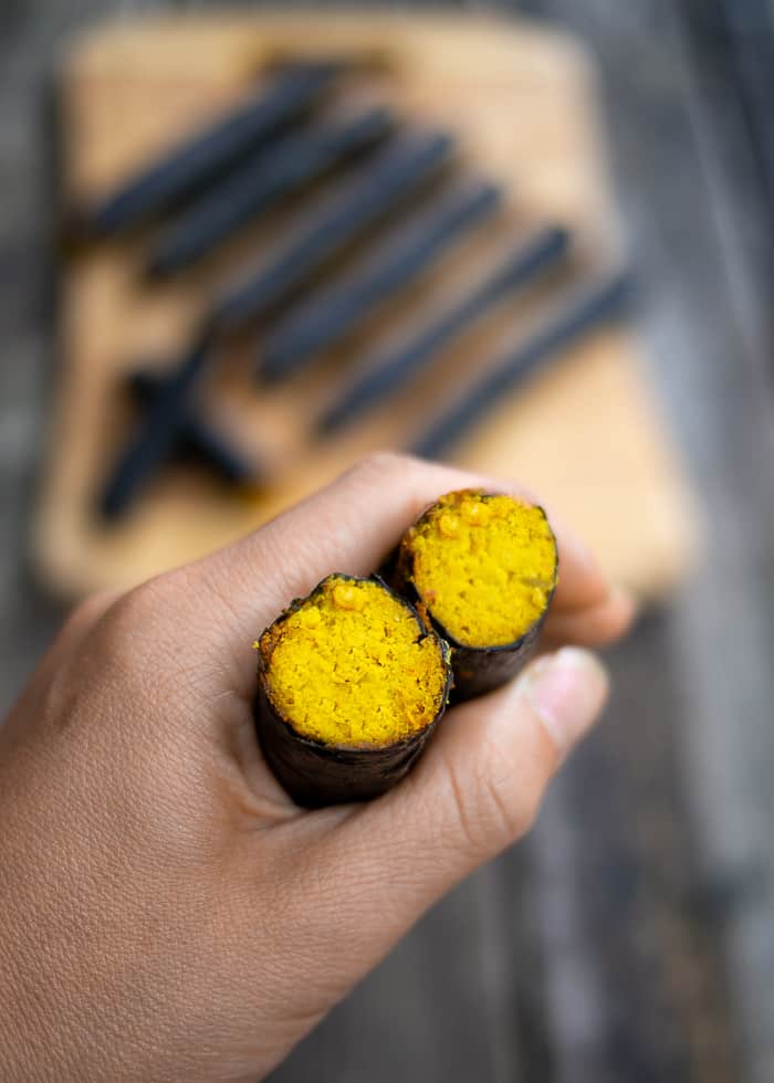 Hand Holding Nori Rolls with Turmeric Carrot and Nuts