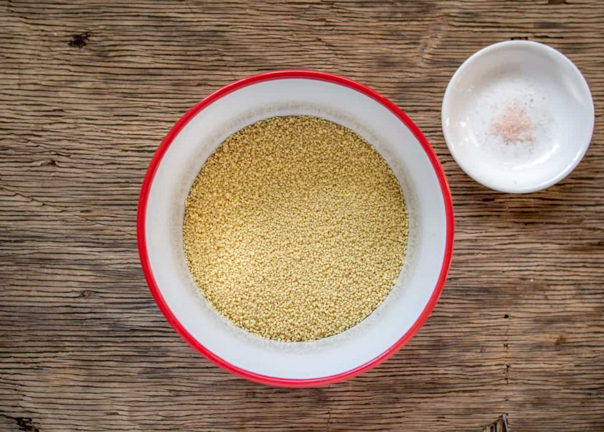 Dry couscous in white and red bowl with salt on the side