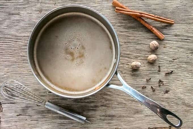 A saucepan with ingredients for pumpkin spiced latte with a whisk to blend well.