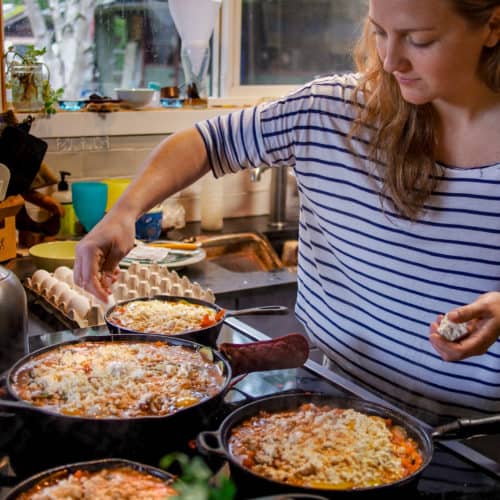 Girl in stripped shirt sprinkling cheese on cast iron shakshouka