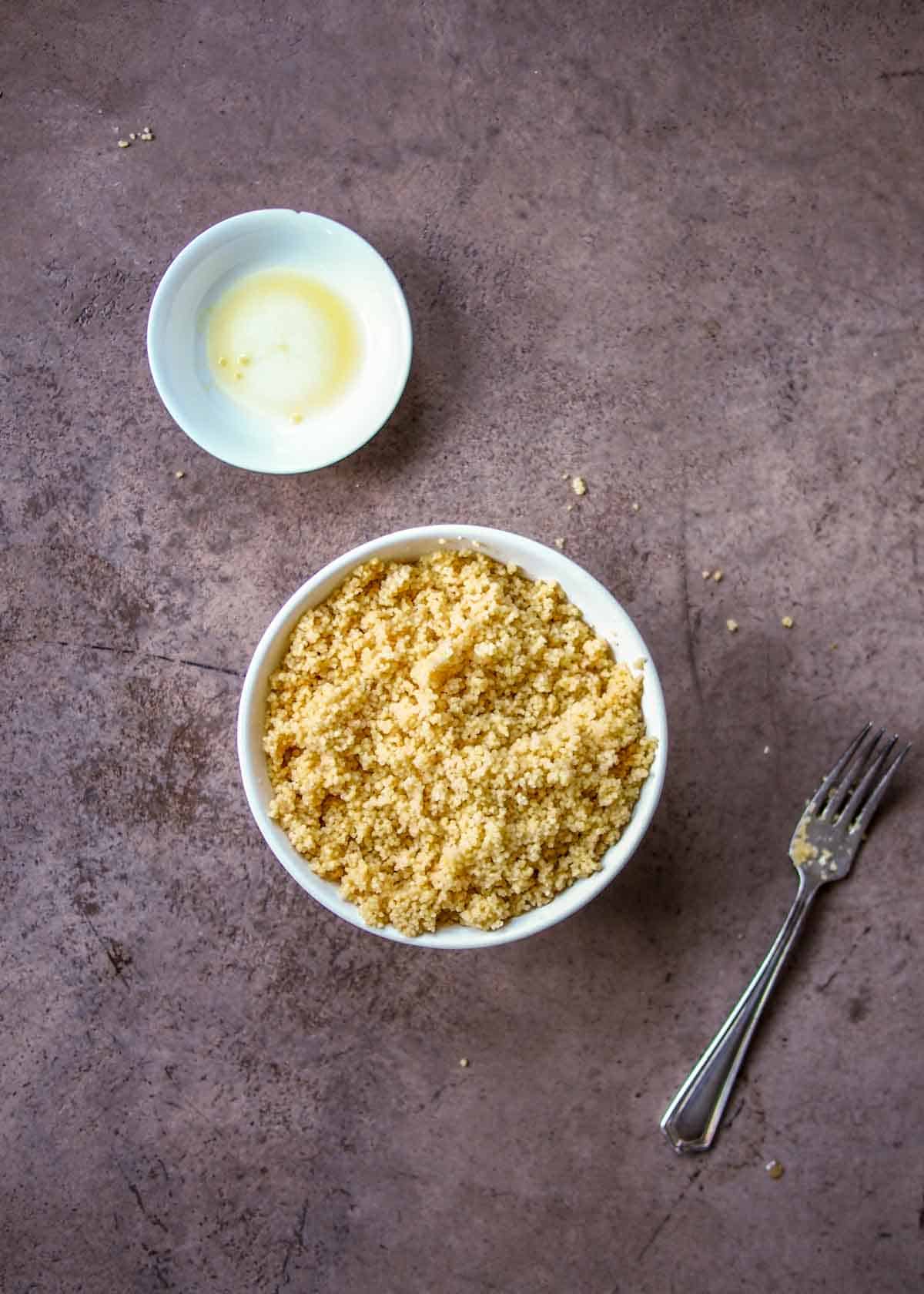 Couscous Fluffed With Fork and Bowl of Oil On Side